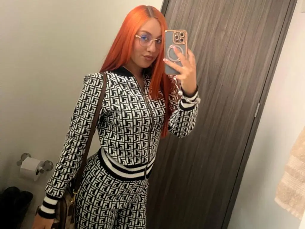 emmawatBuddy — Woman with bright orange hair in a black and white geometric patterned tracksuit taking a mirror selfie.