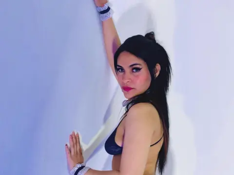 Young woman in black bikini bra posing against a white wall with a confident and moody expression.