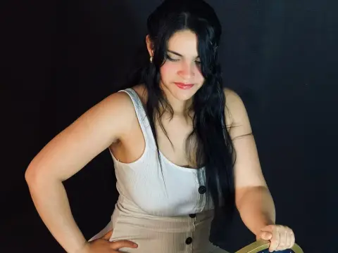 Young woman with long dark hair wearing a white ribbed tank top against a black background.
