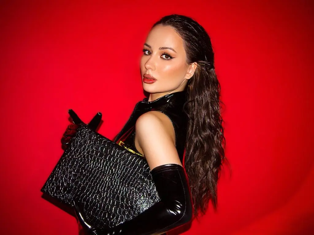 MissBelle — Glamorous woman in chic black leather outfit and gloves holding a textured clutch against a bold red background.