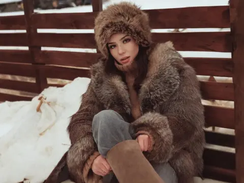 Stylish woman in a brown faux fur coat and fluffy hat sitting on a wooden bench in a snowy winter setting.