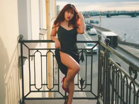 ErikaKim — ErikaKim poses on a balcony wearing a short black slip dress and red heels, showing off her long legs against a river and city background.