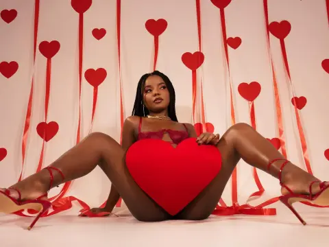 Young woman in red lingerie holding a large heart against a romantic Valentine's Day backdrop.
