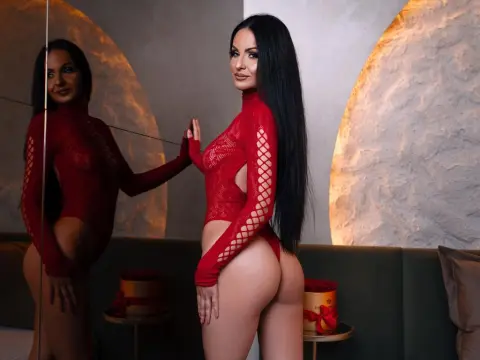 Woman in a red long-sleeve lace bodysuit posing in a modern room with warm lighting.