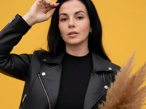 Stylish woman in a black leather jacket and turtleneck posing against a bright yellow background.