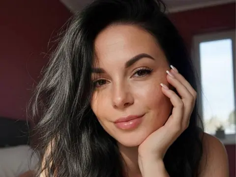 Smiling woman with long dark hair in a sunlit room, featuring a natural and serene facial expression.