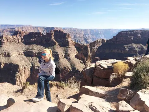 Exclusivegirl — Smiling blonde woman in a grey hoodie and jeans enjoying the sunny view at the Grand Canyon rim.