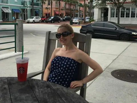 Exclusivegirl — Smiling woman in a blue patterned strapless top sitting at an outdoor cafe with a red iced drink.