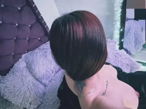Woman with short dark hair sitting on a purple shaggy bed in a cozy bedroom setting.