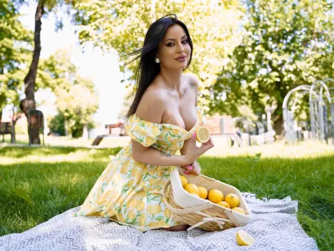 CamileOwnes — CamileOwnes sits on a picnic blanket in a yellow lemon print sundress holding a lemon slice in a park.