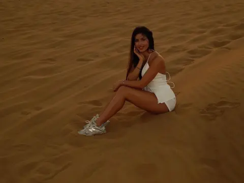EvaBerryy — EvaBerryy sits on a sand dune wearing a white bodysuit and white sneakers, smiling at the camera.