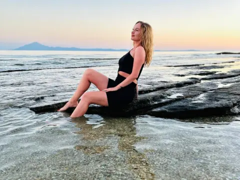 Blonde woman in black swimwear relaxing on coastal rocks at sunset by the calm ocean water.
