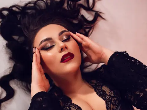 RavenKathe lies back with her eyes closed, wearing a black lace top and heavy eye makeup with red lipstick, her dark hair spread out behind her.