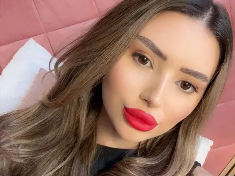 Woman with long brown hair and bold red lipstick posing against a pink tufted headboard in a soft mood.