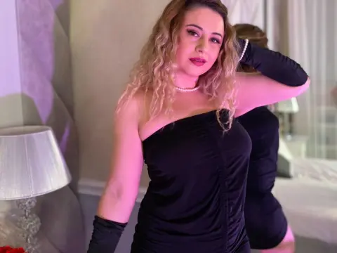 Glamorous woman in a black strapless dress and long gloves posing in a soft-lit bedroom setting.