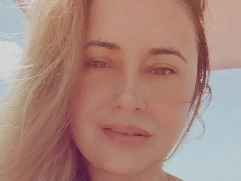 Close-up portrait of a smiling woman with blonde hair outdoors in bright natural sunlight.
