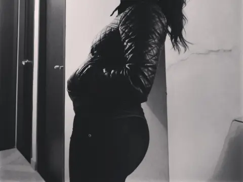 Brona_Sexy — Moody black and white portrait of a woman in a quilted leather jacket standing against a minimalist wall.
