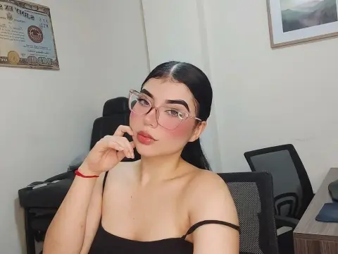 Young woman with glasses and black tank top posing in a home office setting with a thoughtful mood.