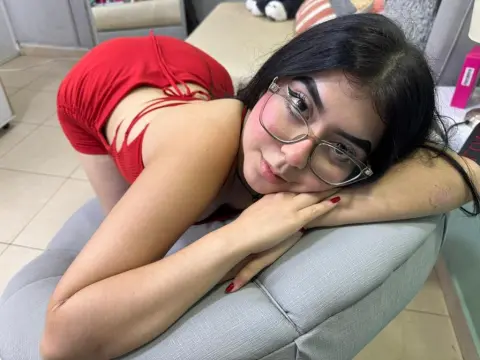Smiling young woman with glasses in a red outfit relaxing on a grey sofa in a bright room.