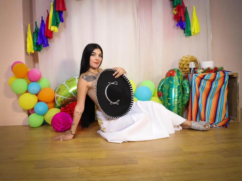 Smiling woman in white dress sitting on floor with colorful balloons and festive decorations.