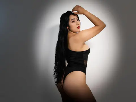 Sara_Rey — Sara_Rey poses in a black bodysuit with her long dark hair flowing down her back against a grey background.