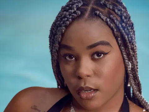 AshantyHopsom looks into the camera with a serious expression, showing off her long silver and black braids against a blue background.