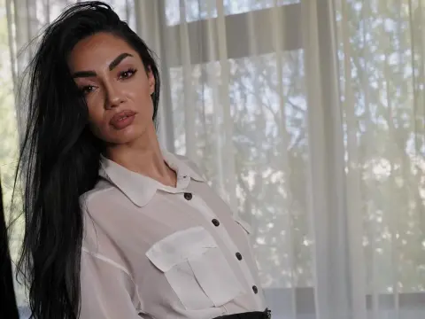 Elegant woman with long dark hair wearing a white button-down shirt in a bright, airy room.