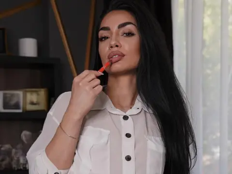 Young woman with long dark hair applying red lipstick while wearing a white button-down shirt in a bright room.