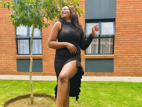 Smiling woman in a black long-sleeve dress posing by a tree in a sunny garden setting.
