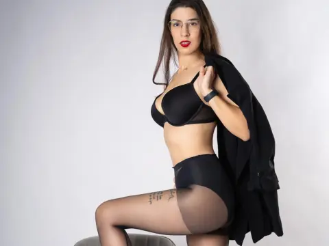 Confident woman in black lingerie and glasses posing against a white background.