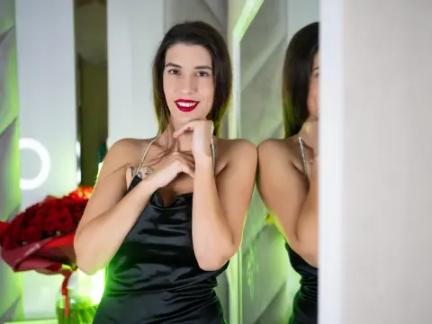 Smiling woman in a black satin dress with red lipstick posing near roses in a modern room.