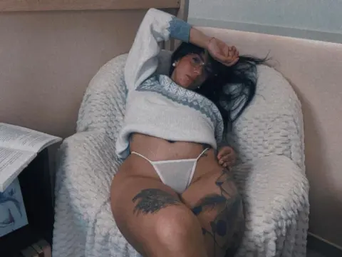 Tattooed woman in a white sweater and bikini relaxing in a cozy armchair for a moody lifestyle shot.