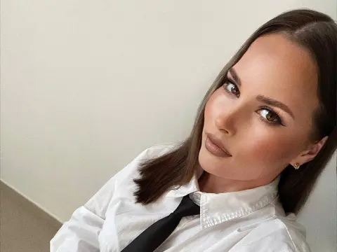 Elegant woman in a white shirt and black tie posing with a sophisticated look against a neutral background.