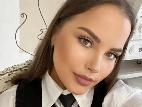 Beautiful woman with elegant makeup wearing a white shirt and black tie in a bright indoor setting.