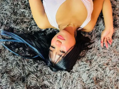 Young woman with long dark hair in a white top lying on a grey shag rug in a relaxed mood.