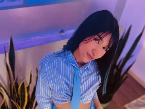 Young woman in a blue striped shirt and tie posing in a room with indoor plants and purple lighting.