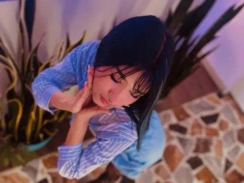 Young woman in a blue striped shirt posing thoughtfully near indoor plants in a moody, purple-lit room.