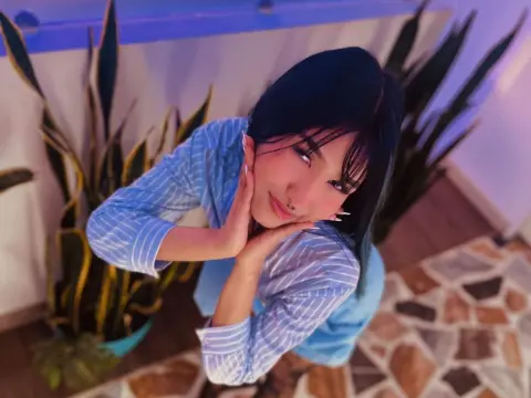 Young woman in blue striped shirt posing playfully near indoor plants in a moody, purple-lit room.