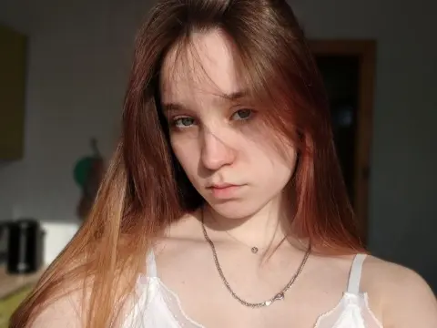 Young woman with long reddish hair wearing a white lace camisole in soft, warm sunlight.
