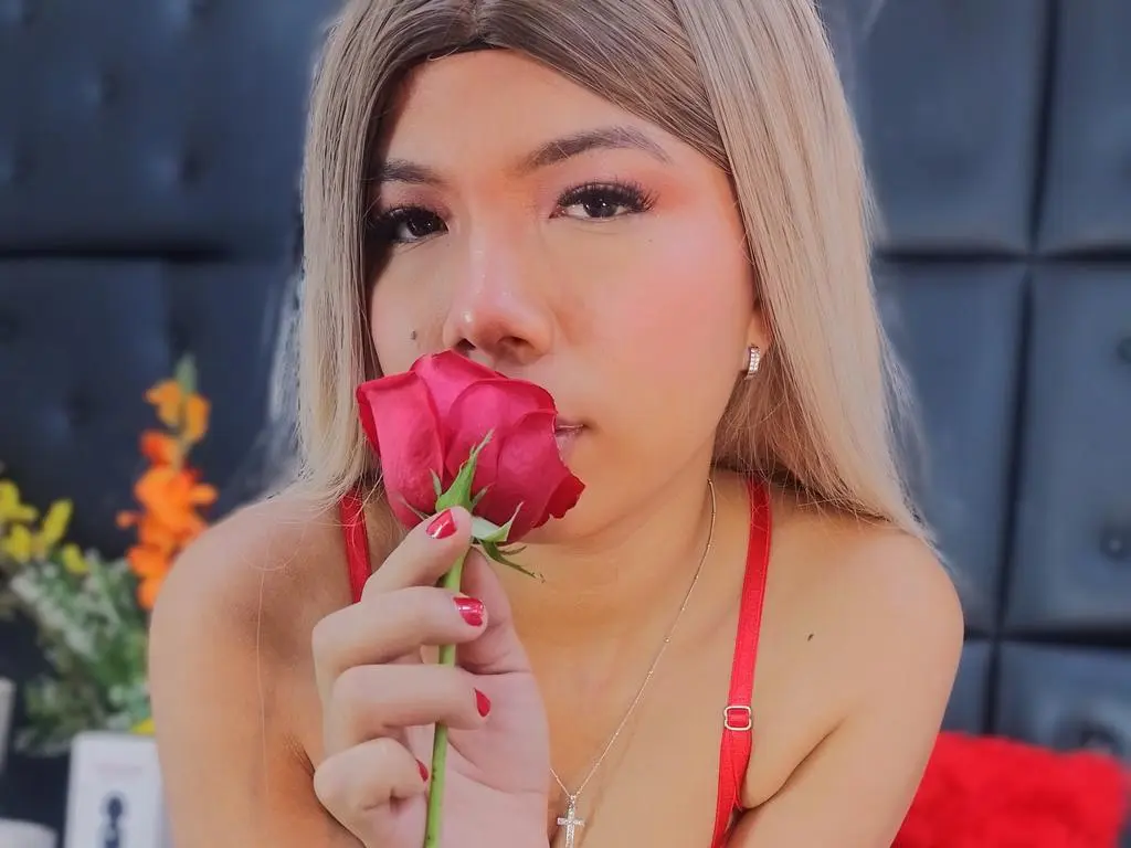 Clloelombaard — Clloelombaard holds a red rose to her lips while wearing a red strap top and a silver necklace.