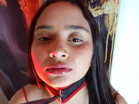 Close-up portrait of a young woman with long dark hair wearing a red and black strap outfit in warm lighting.