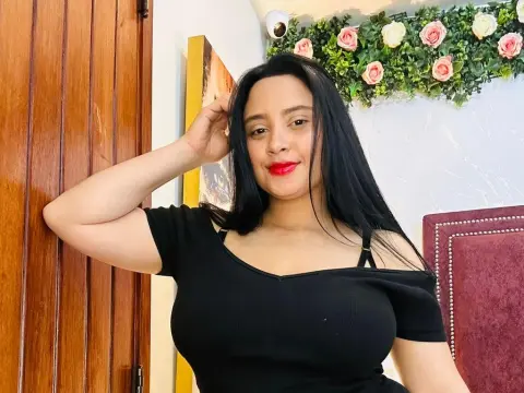 Smiling woman in a black v-neck top posing against a floral wall and wooden door in a bright room.