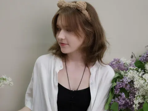 YukiPage — YukiPage wearing a white shirt and a fuzzy headband, posing next to purple lilac flowers.