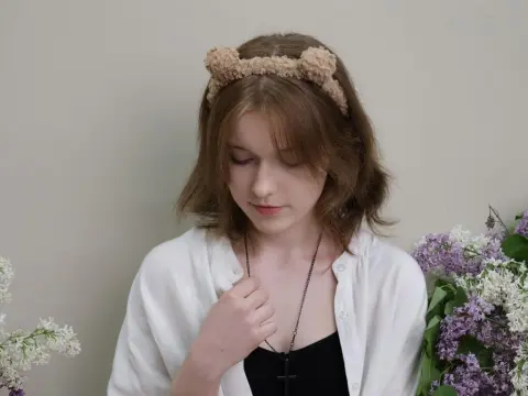 YukiPage wears a white shirt and a fuzzy headband while looking down in front of purple flowers.