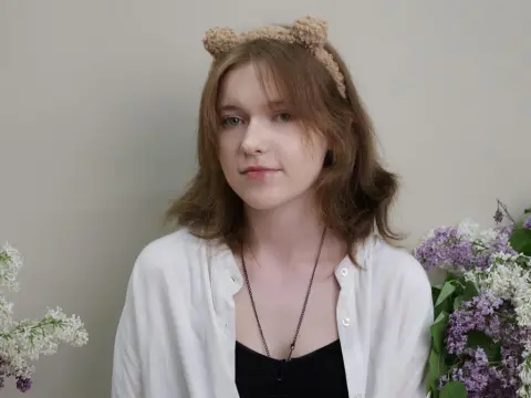 YukiPage wears a white shirt and a fuzzy cat-ear headband while posing next to purple lilac flowers.