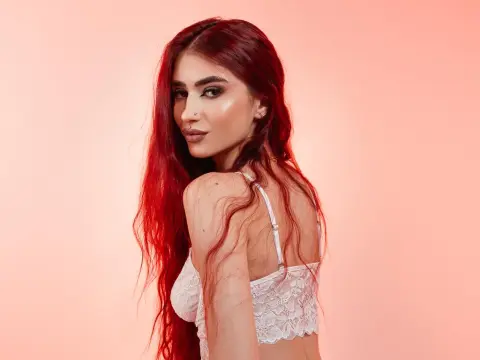 VixenRose — Beautiful woman with long red hair wearing white lace lingerie against a soft pink background.