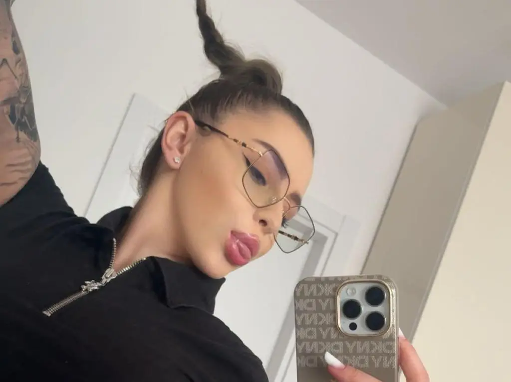 IvySins — IvySins pouts her lips while wearing large glasses and a black collared shirt, taking a mirror selfie with her phone.
