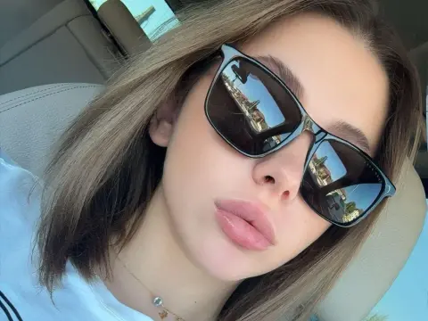 IvySins — IvySins wearing large black sunglasses and a white t-shirt, posing in a car with her light brown hair down.