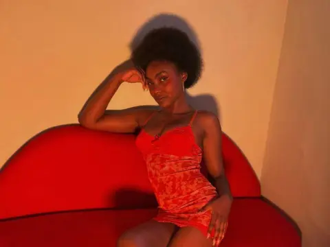 Asha_zuri69 poses on a red couch wearing a red lace slip, resting her head on her hand with her hair in an afro.
