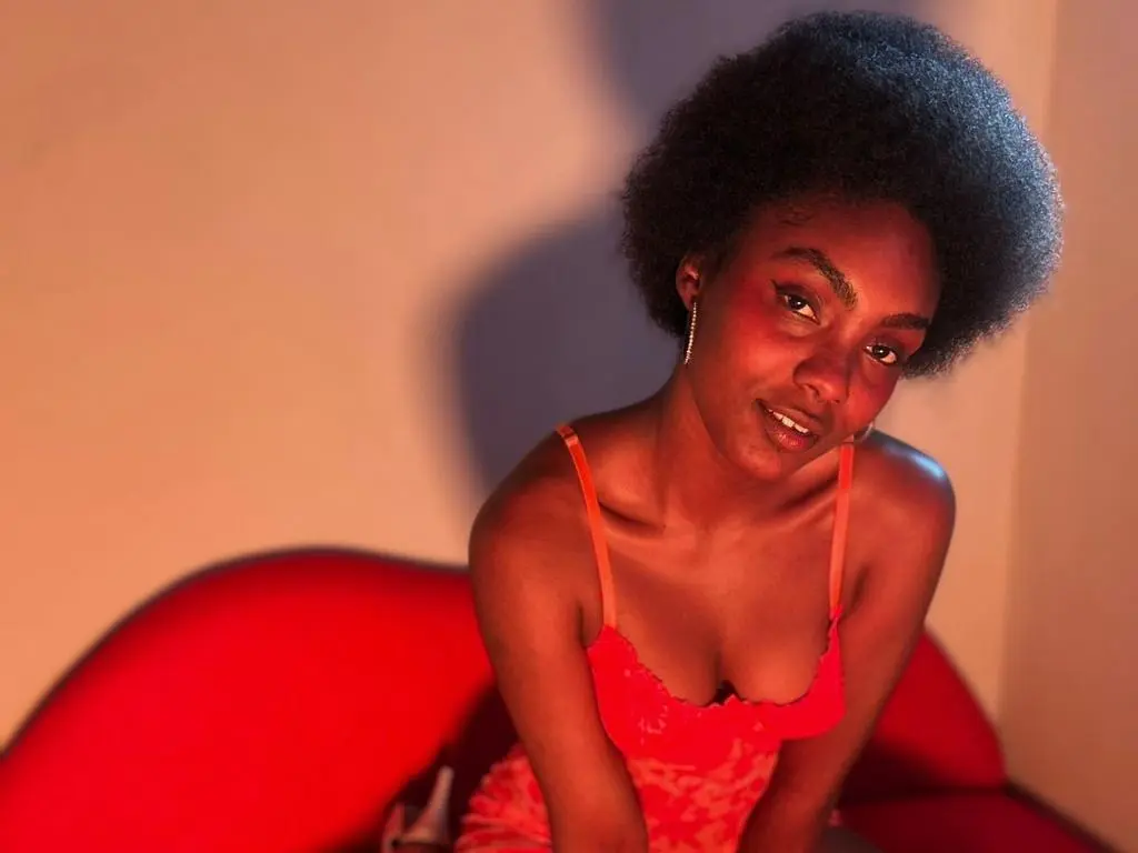 Asha_zuri69 — Asha_zuri69 wearing a red lace camisole, posing with her hair in an afro while sitting on a red sofa.